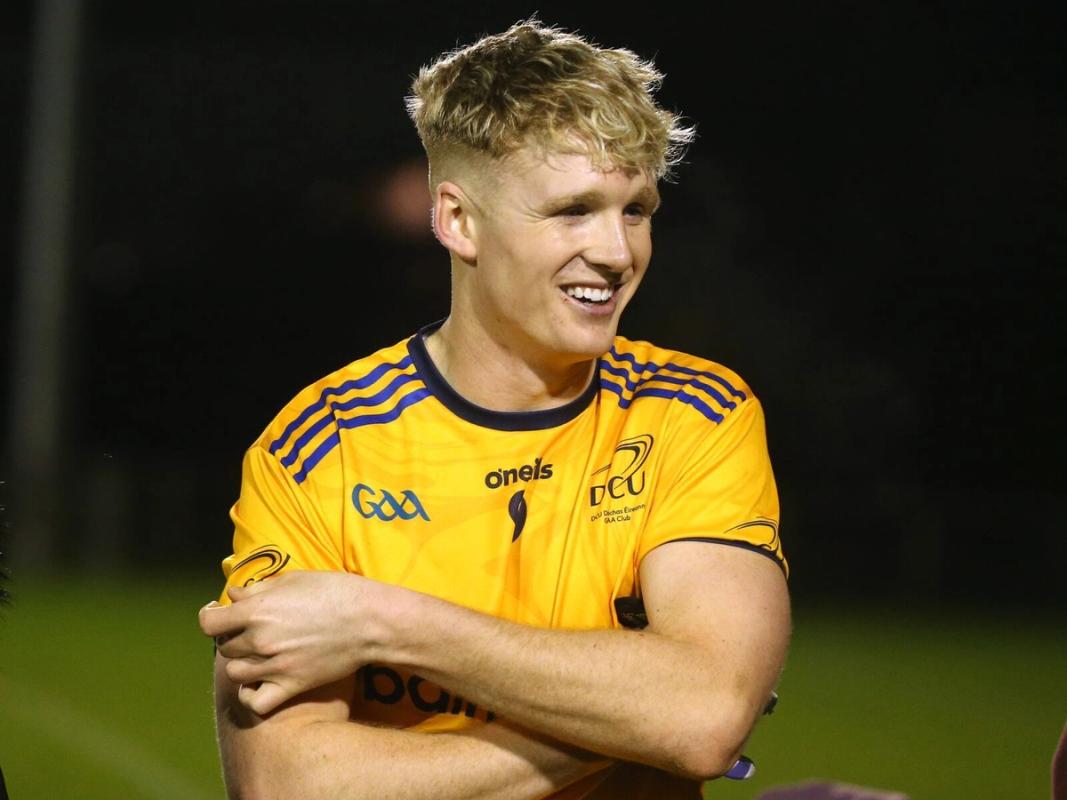 A young man in a yellow football jersey is smiling and looking off camera