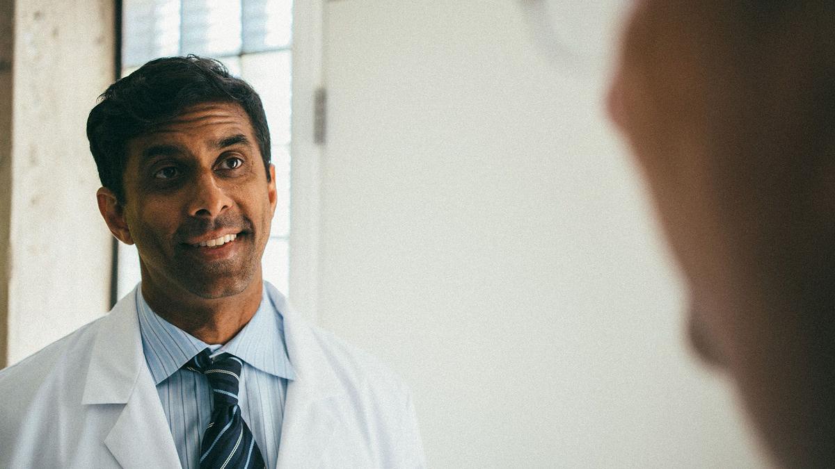 Photo of trustworthy-looking doctor in white medical coat, talking to camera.