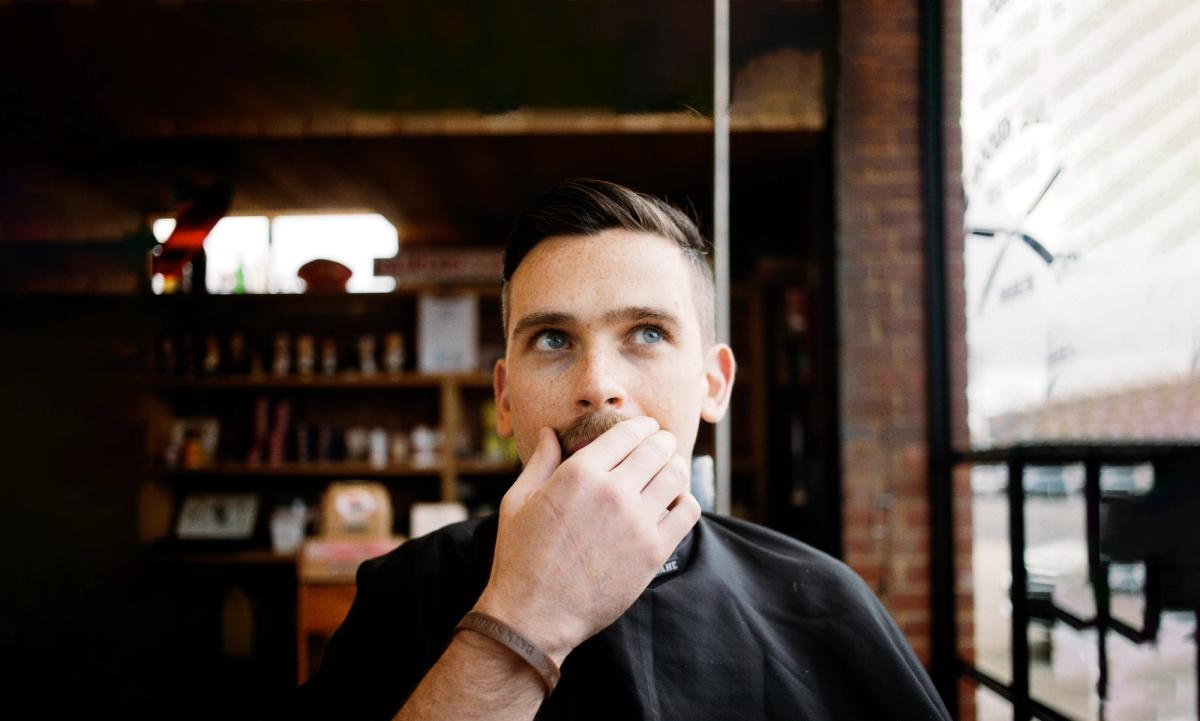 A man in a barber chair is stroking his moustache.