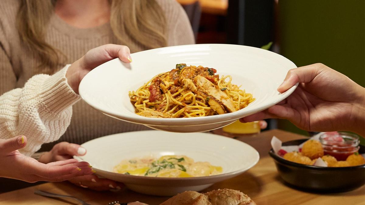 A plate of pasta gets passed across a table full of lovely Italian dishes.