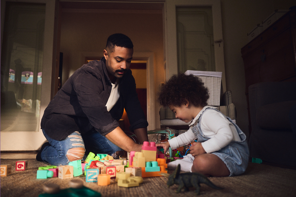A dad is sitting on the floor playing with blocks with his young toddler