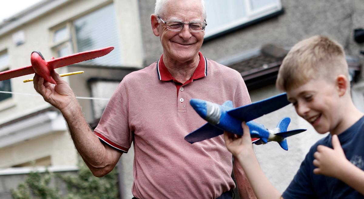 A grandfather and grandson play together with model airplanes, they are smiling and laughing
