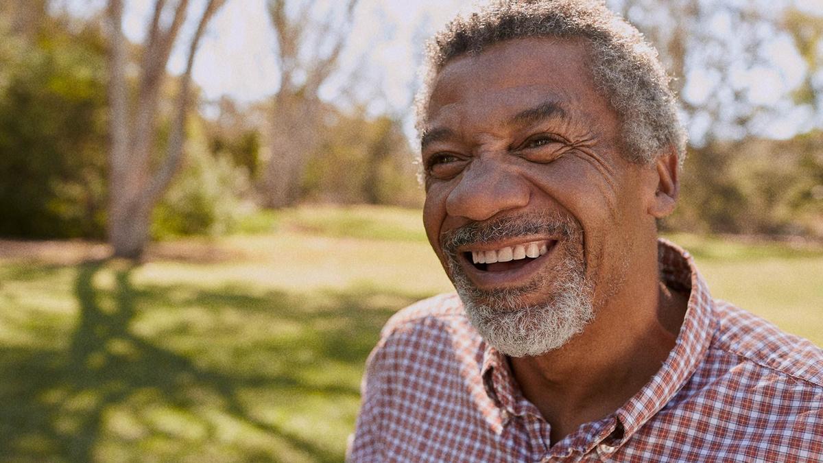 A mature-aged Black man smiling while looking past the camera.