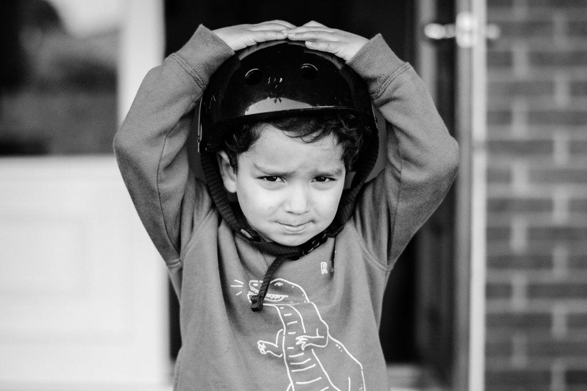 A young boy wearing a helmet looks worried, with both hands on top of his head.