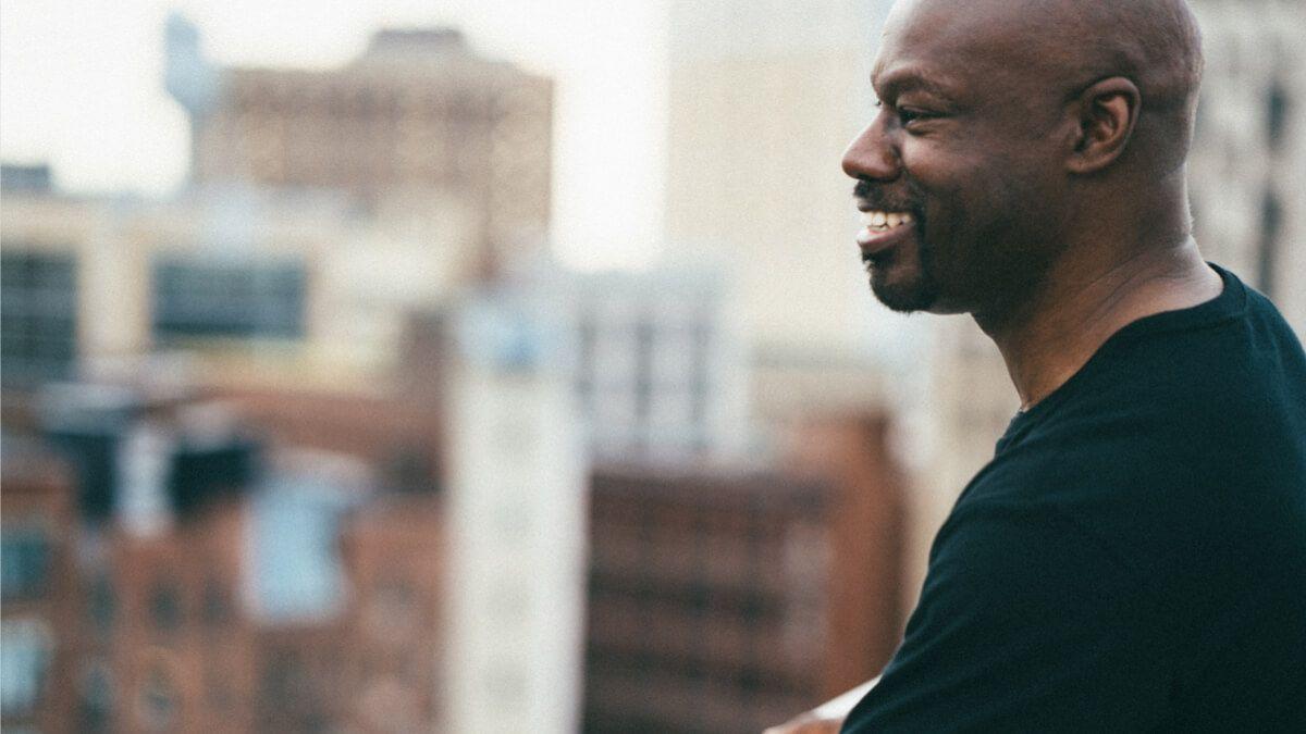  Black man looking out at city buildings from balcony