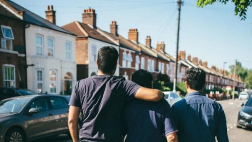 Three men walking down the street with their backs towards the camera and arms around each other