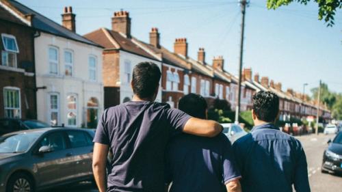 Three men walking down the street with their backs towards the camera and arms around each other