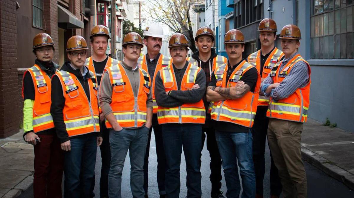 A group of construction workers in high vis vests and helmets pose for the camera
