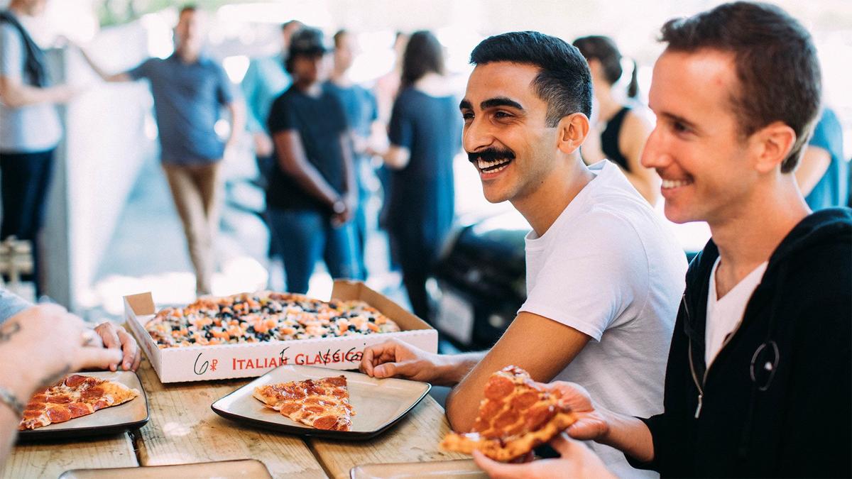 An image of two Mo Bros smiling and laughing while eating pizza together.