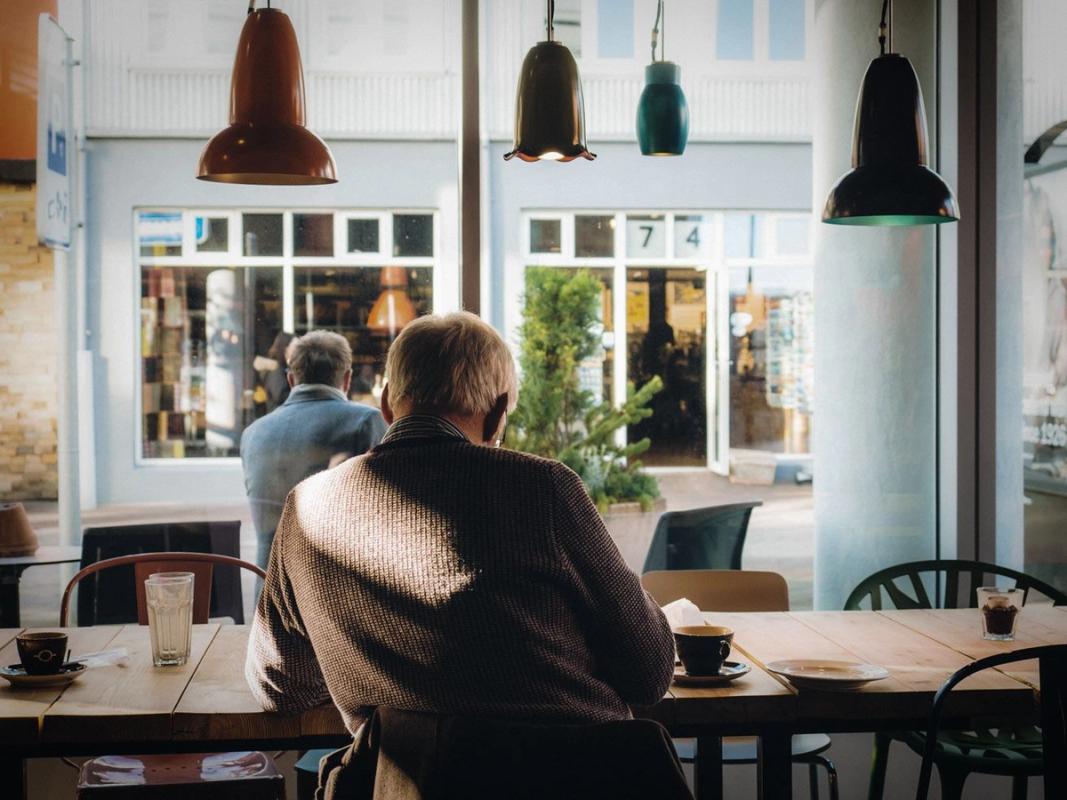 Rear view of older man sitting by himself at a coffee shop.