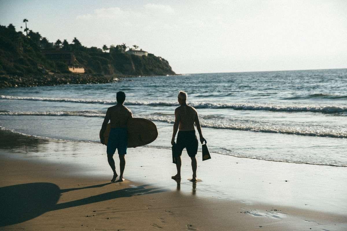 Two men with a surfboard walking on beach