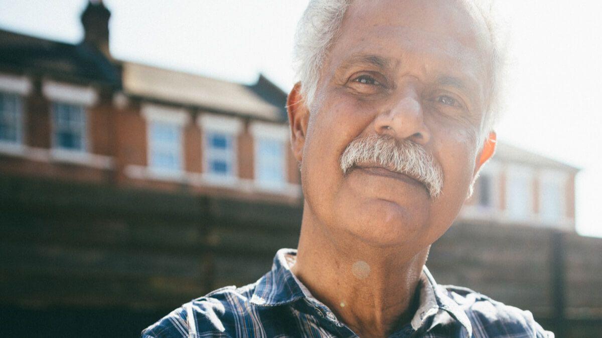 Older man with moustache standing in front of a row of houses