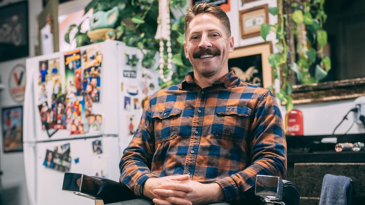 A man smiles for a photo while sitting in a barber chair