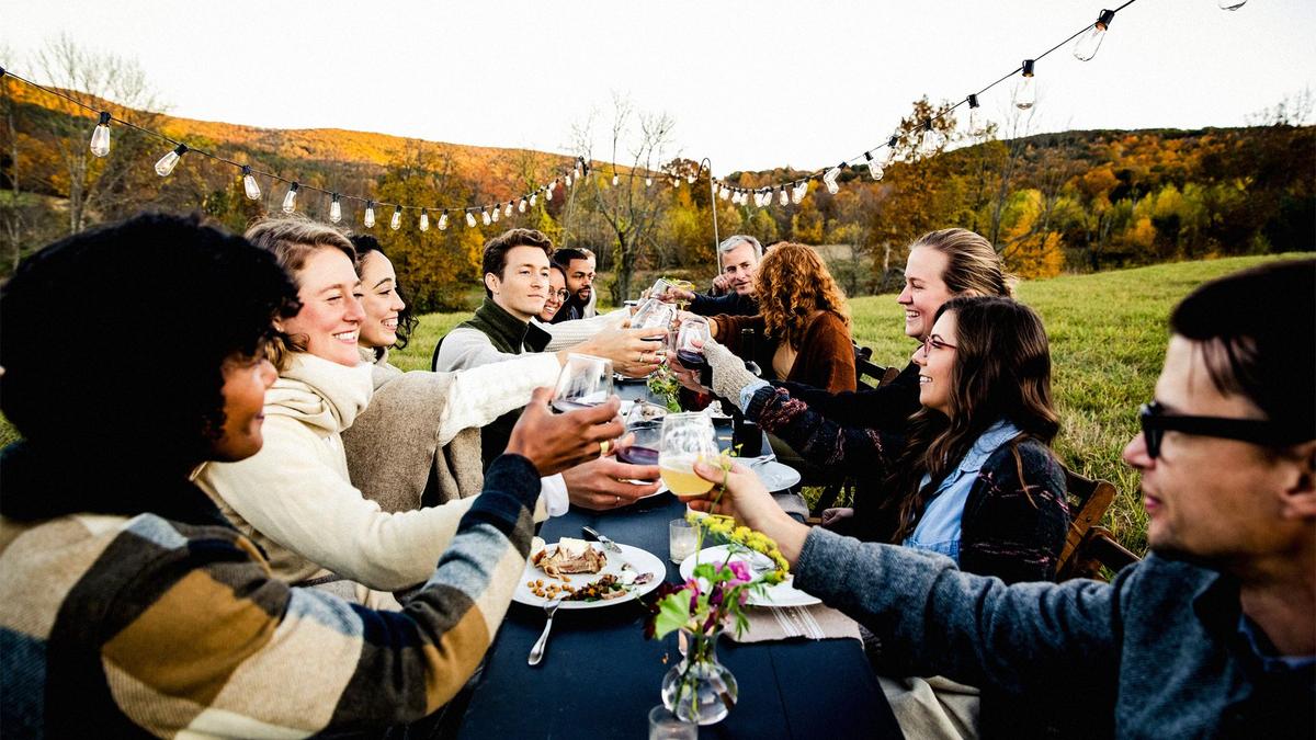 A group of people gathered around a long dinner table at a fall feast