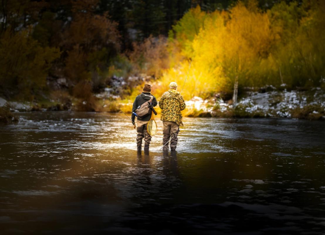 Two men standing side by side wading into a shallow river