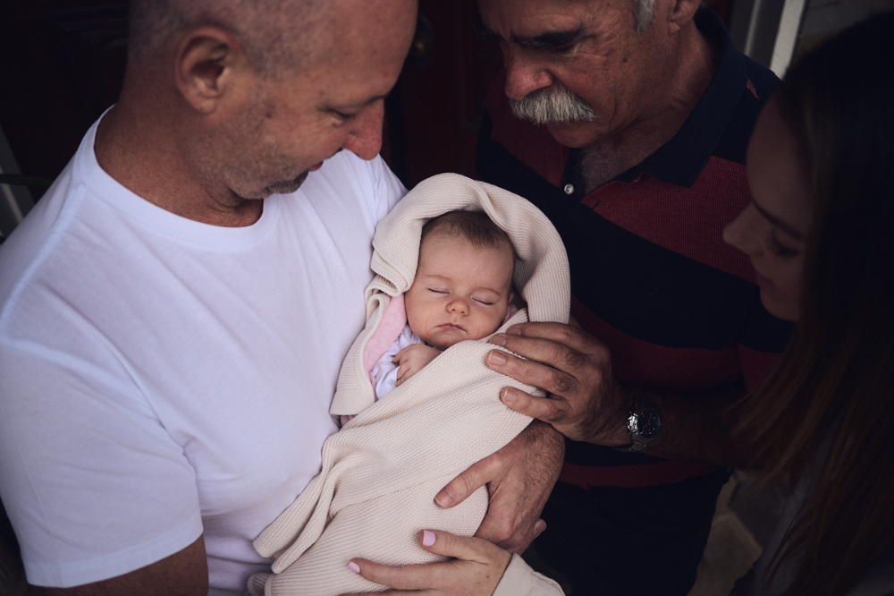 Two men and a woman are cuddled around a swaddling sleeping baby