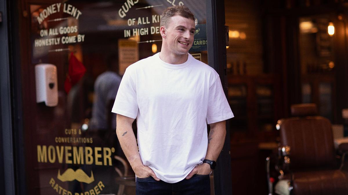 A photograph of a man standing outside a barber shop