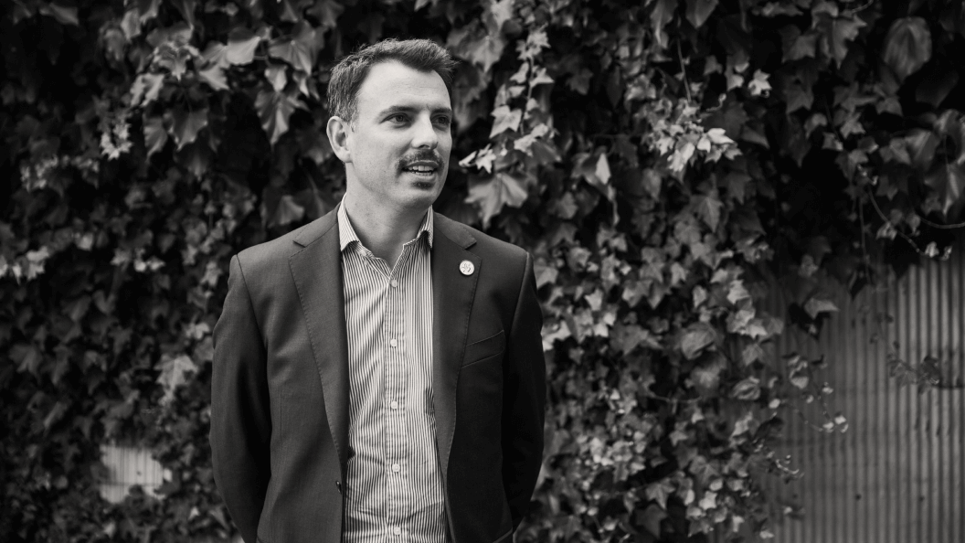 Young man in casual suit standing against a wall of vines