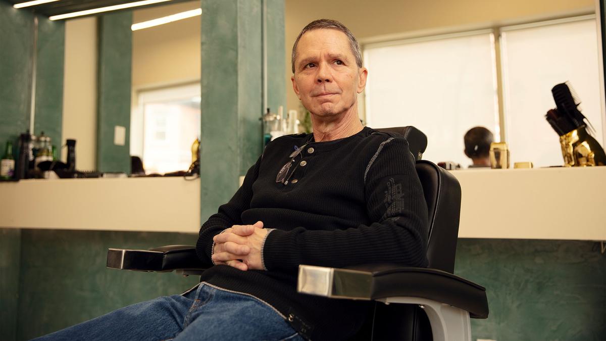 A smiling and pensive man in his 60's poses for a portrait in a barber chair
