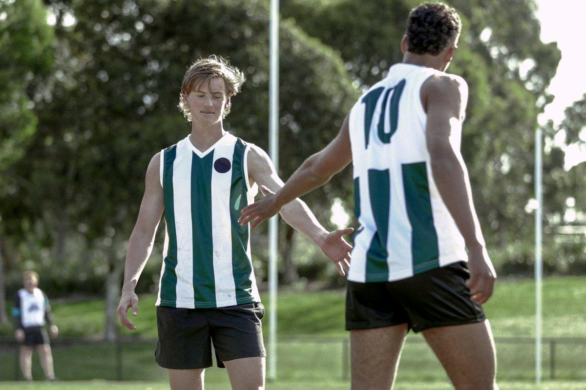 Two young AFL players on the field, one reaching out to the other after a tough moment in the game.