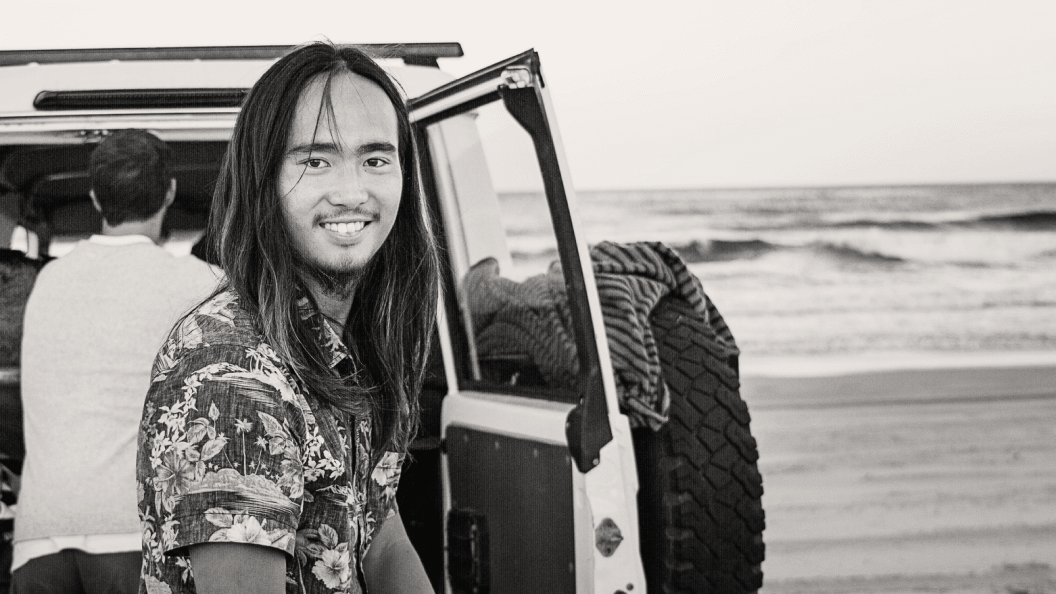 Man with long hair at the beach with a four wheel drive vehicle