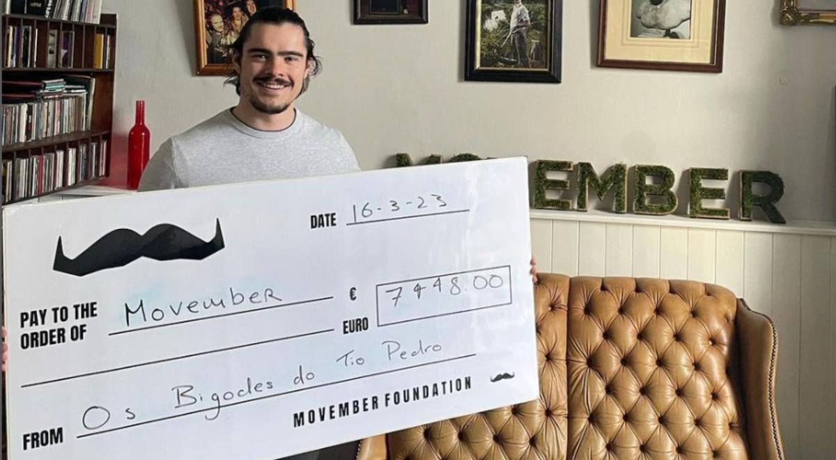 Man standing and holding a giant cheque of 7448 euros for Movember