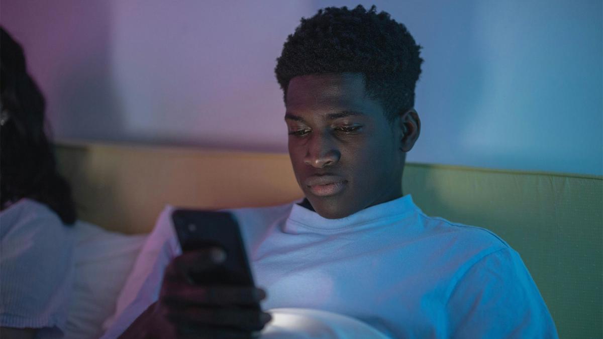 A young man views his smart phone, illuminated by its glow