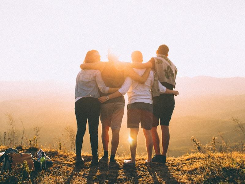 Four people hugging in the outdoors at sunrise
