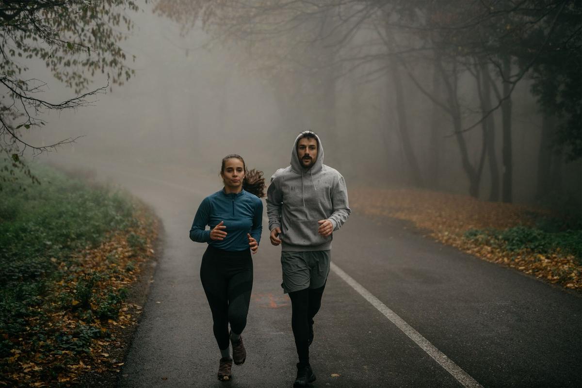 A man and woman running together on a misty tree-lined road in autumn.