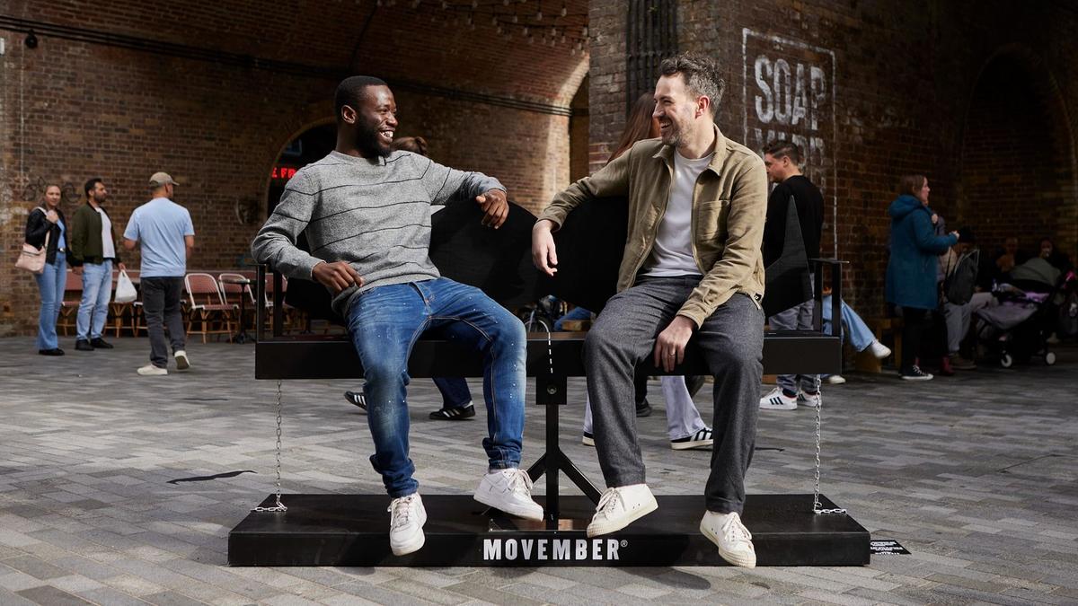 2 men sat on a moustache shaped bench talking