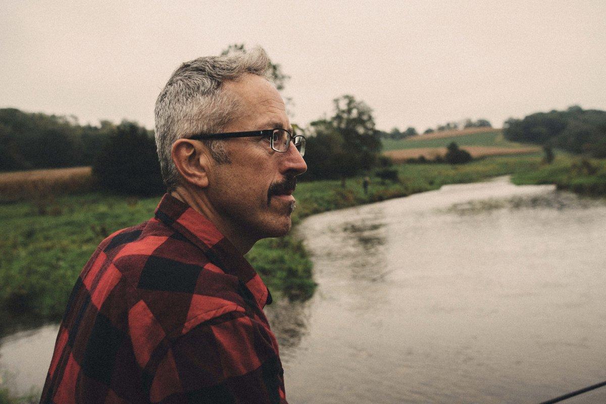 A middle-aged man with a moustache and glasses gazing into the distance on an overcast day.