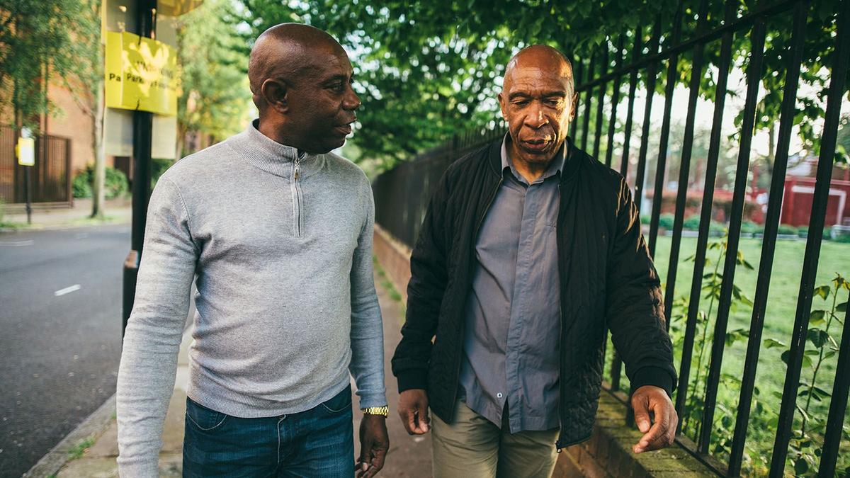 Two middle-aged men walking down suburban street.