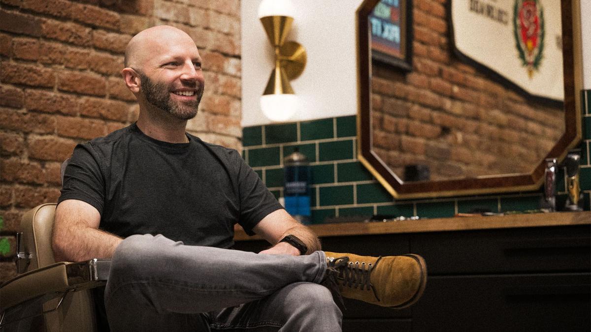 Mo Bro Chris sits casually in a barber chair in a shop in Denver