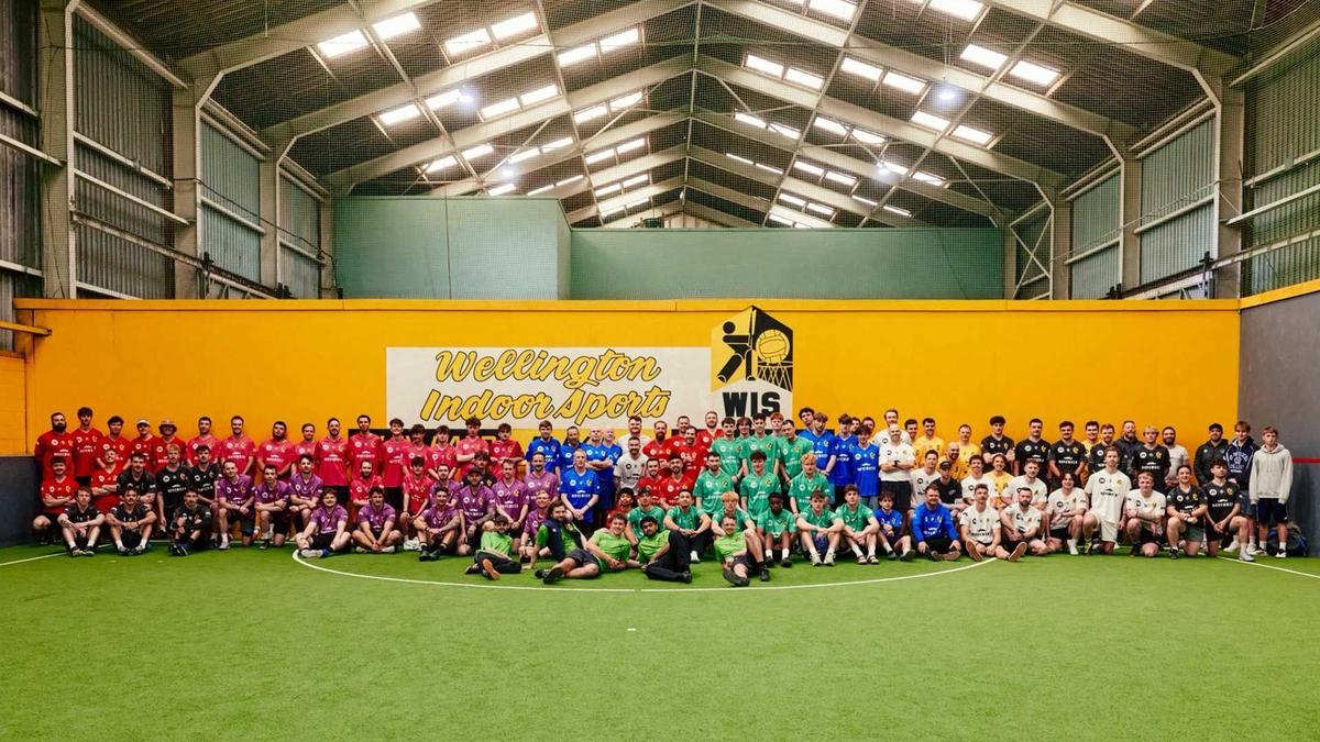 Multiple indoor football players in different coloured kits stand for photo on green indoor football pitch
