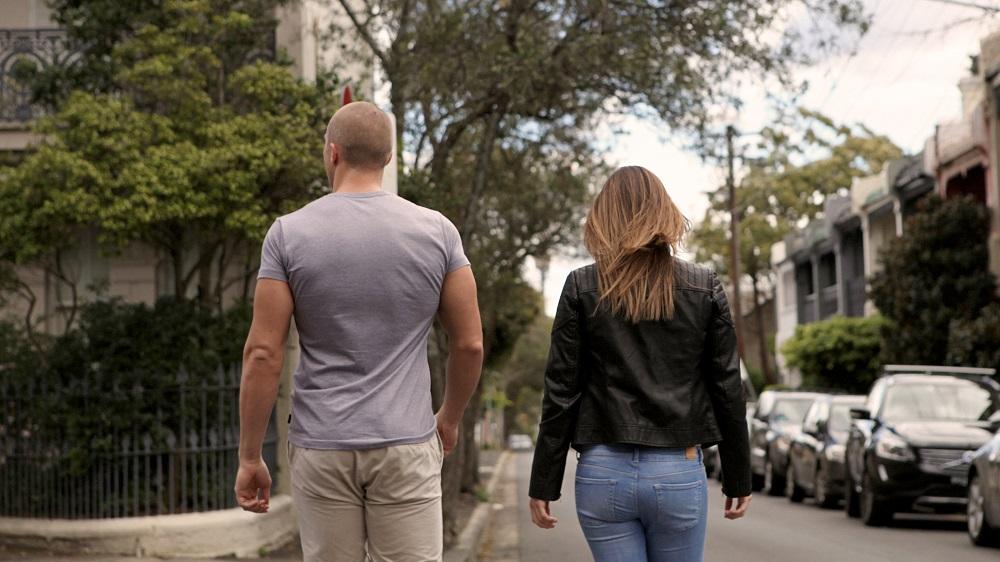 A man and woman walking side by side down a tree-lined street, seen from behind.