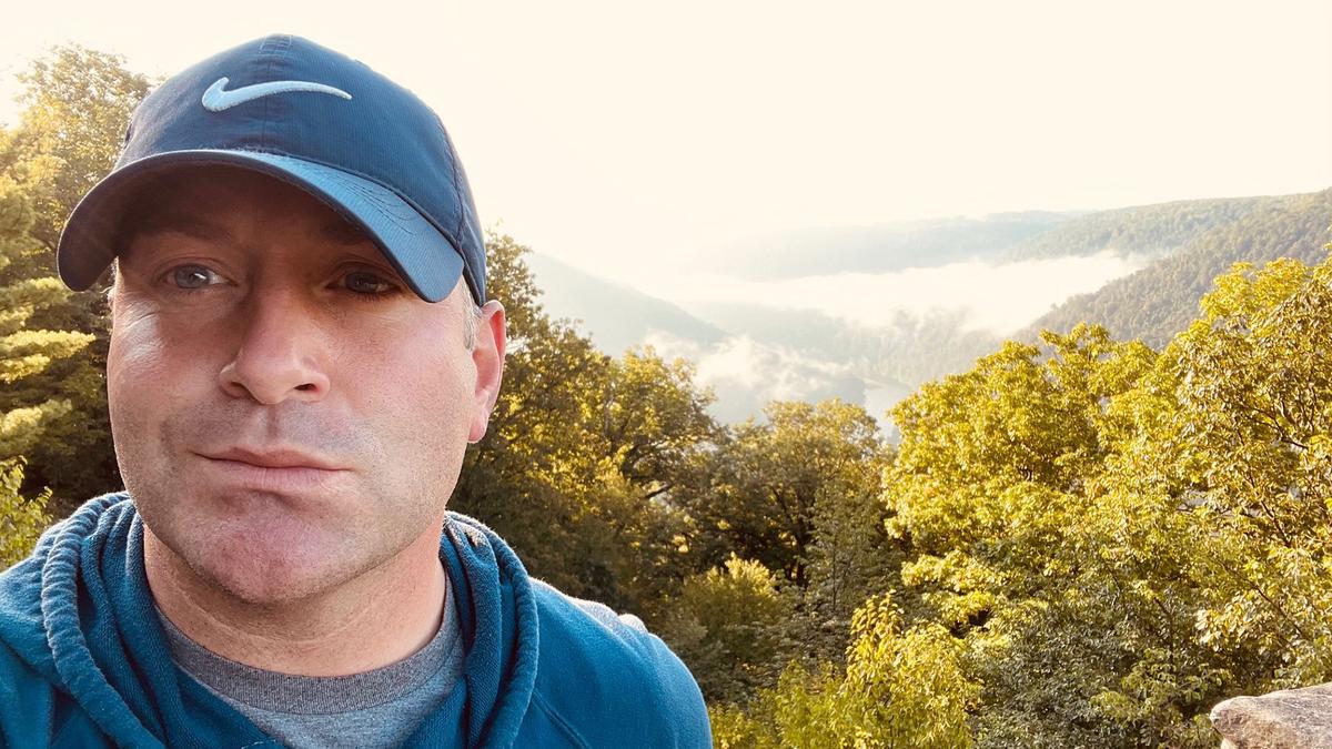 A man smiles in front of an incredible valley of rolling hills and trees in the Appalachian Mountains