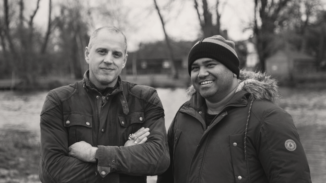 Two men standing together outdoors, smiling.