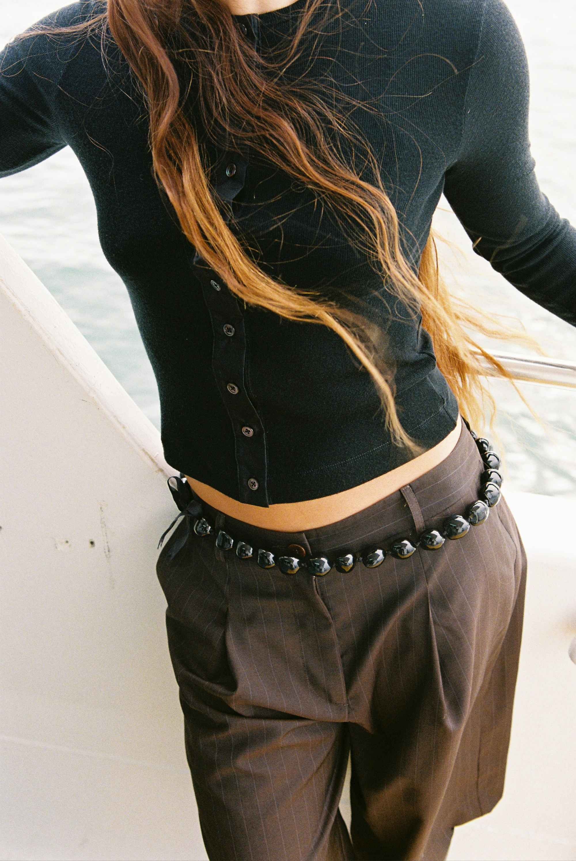 Model with long hair wearing pinstripe shorts and black wool cardigan on a ferry