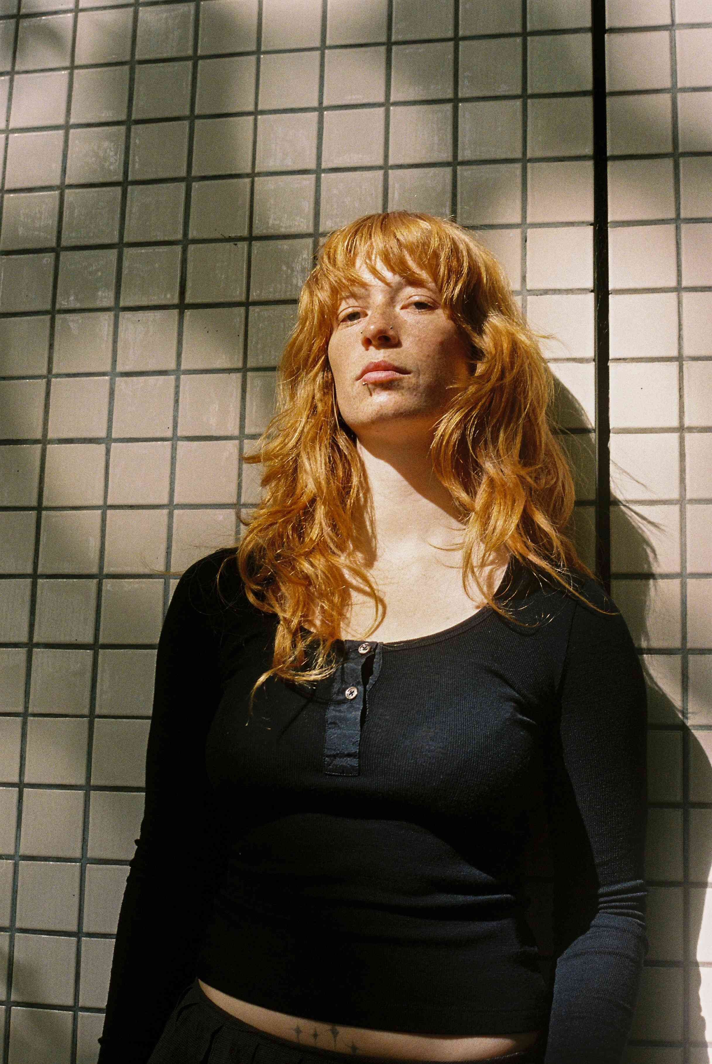 Model leaning against a wall wearing a black knit henley top 