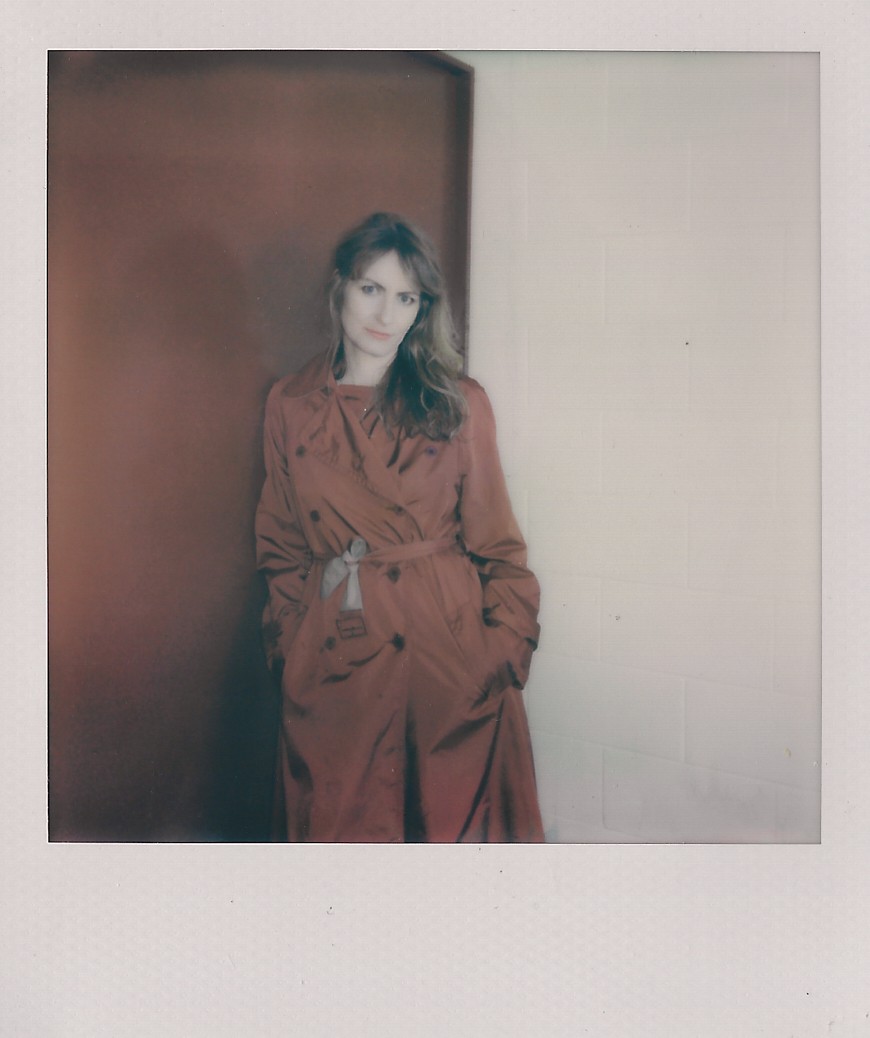 Kate Megaw leaning on the wall in a red trenchcoat