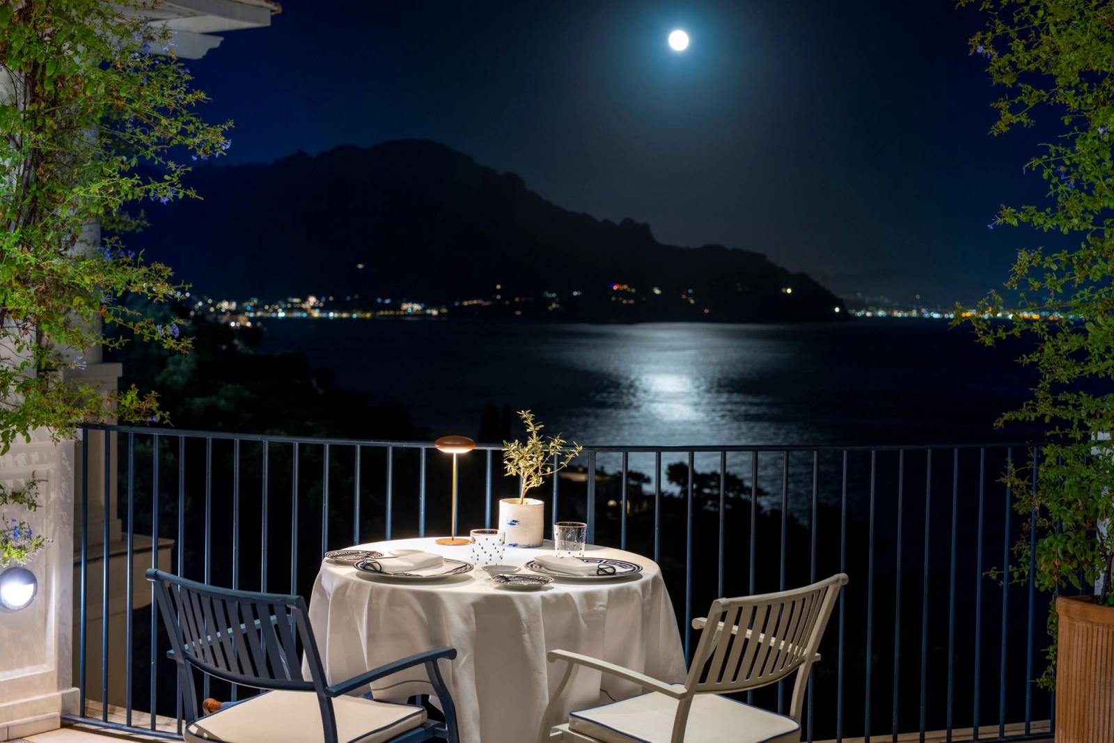 A candlelit terrace above a moonlit Mediterranean bay.