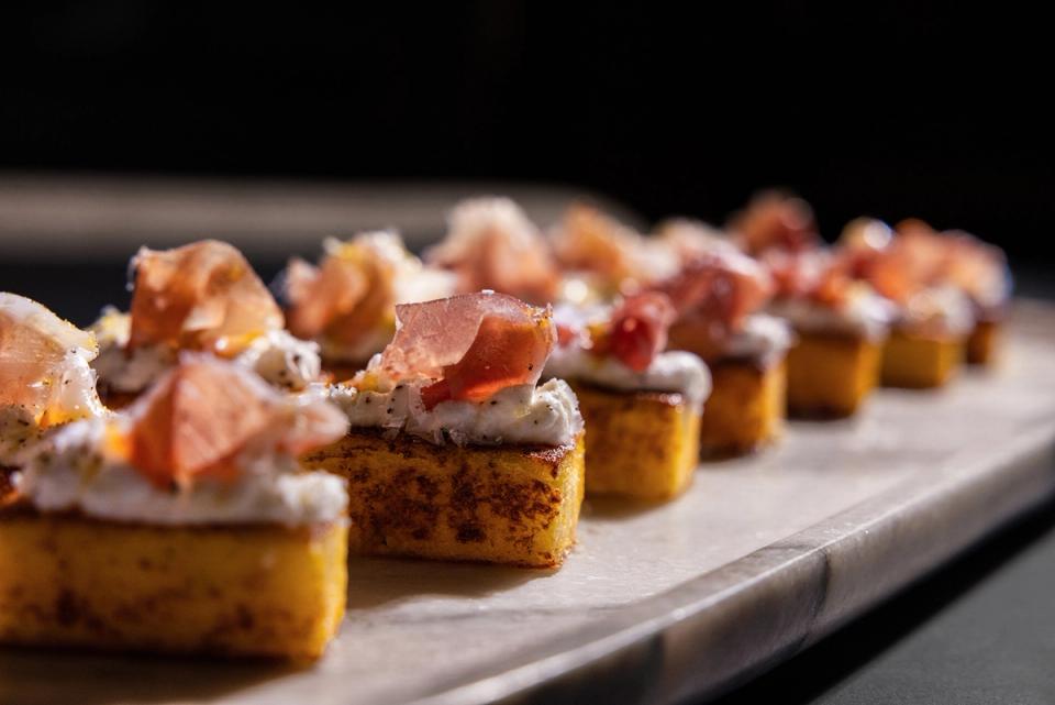 Row of gourmet polenta canapes topped with prosciutto on a marble tray