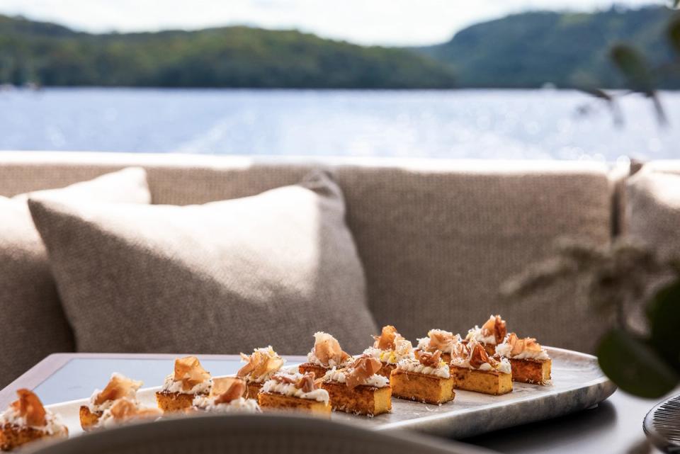 Canapes plated on a tray beside cushioned seating with a lake and hills view