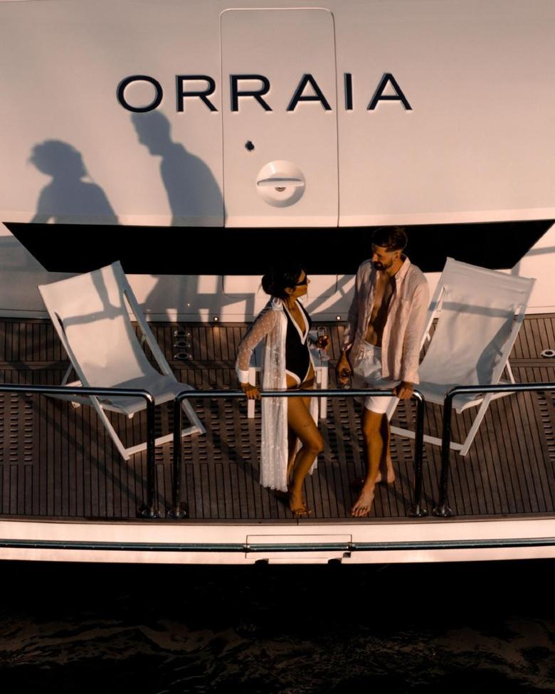 A couple relaxing between deckchairs on the swim platform beneath the ORRAIA name