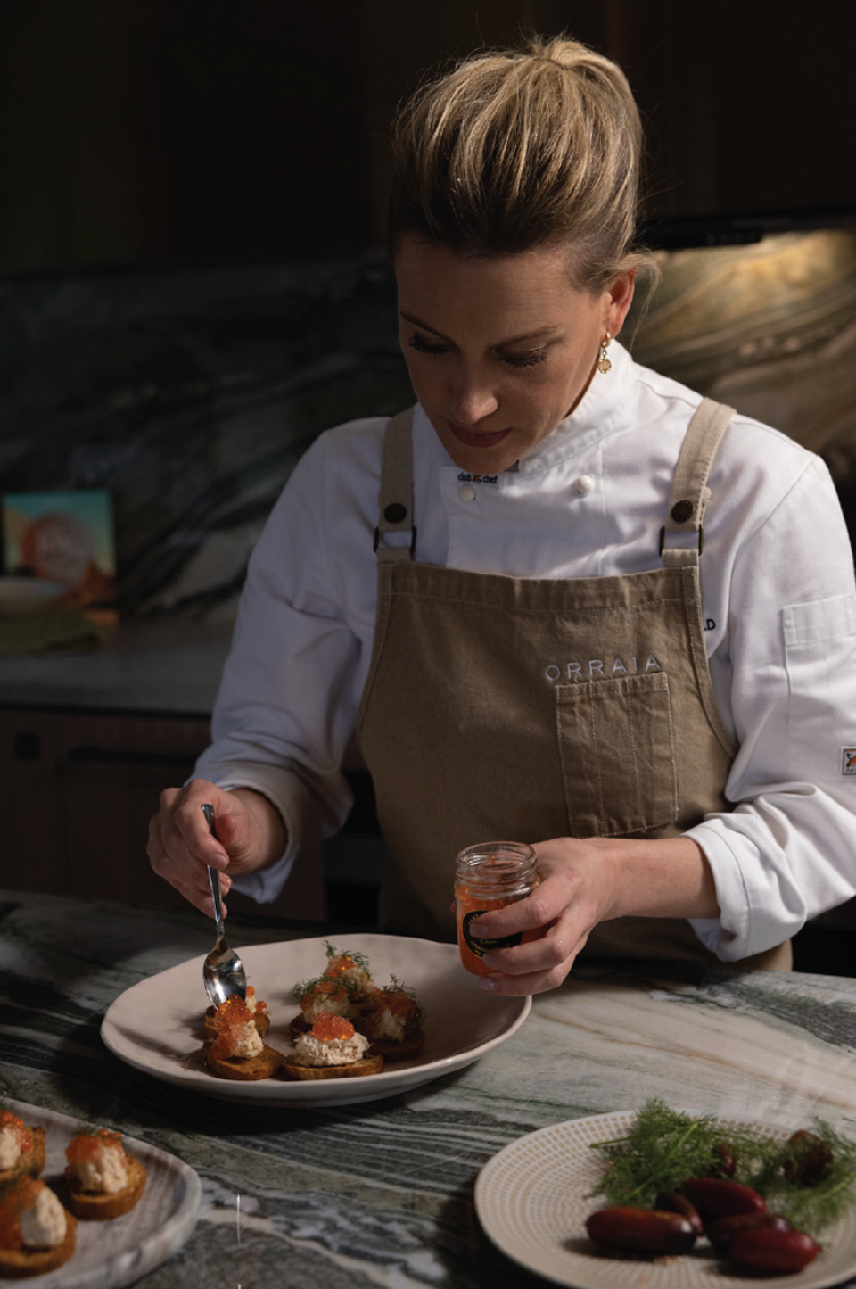 A chef in an ORRAIA apron plating canapes with a spoon of roe
