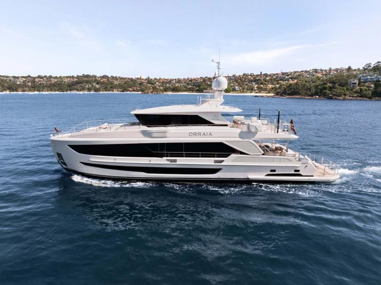 ORRAIA superyacht cruising alongside a coastal headland with houses among trees