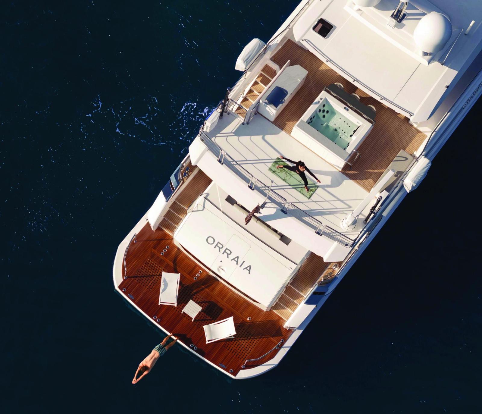 M/Y ORRAIA from directly above, teak decks on deep blue water, a swimmer diving from the stern