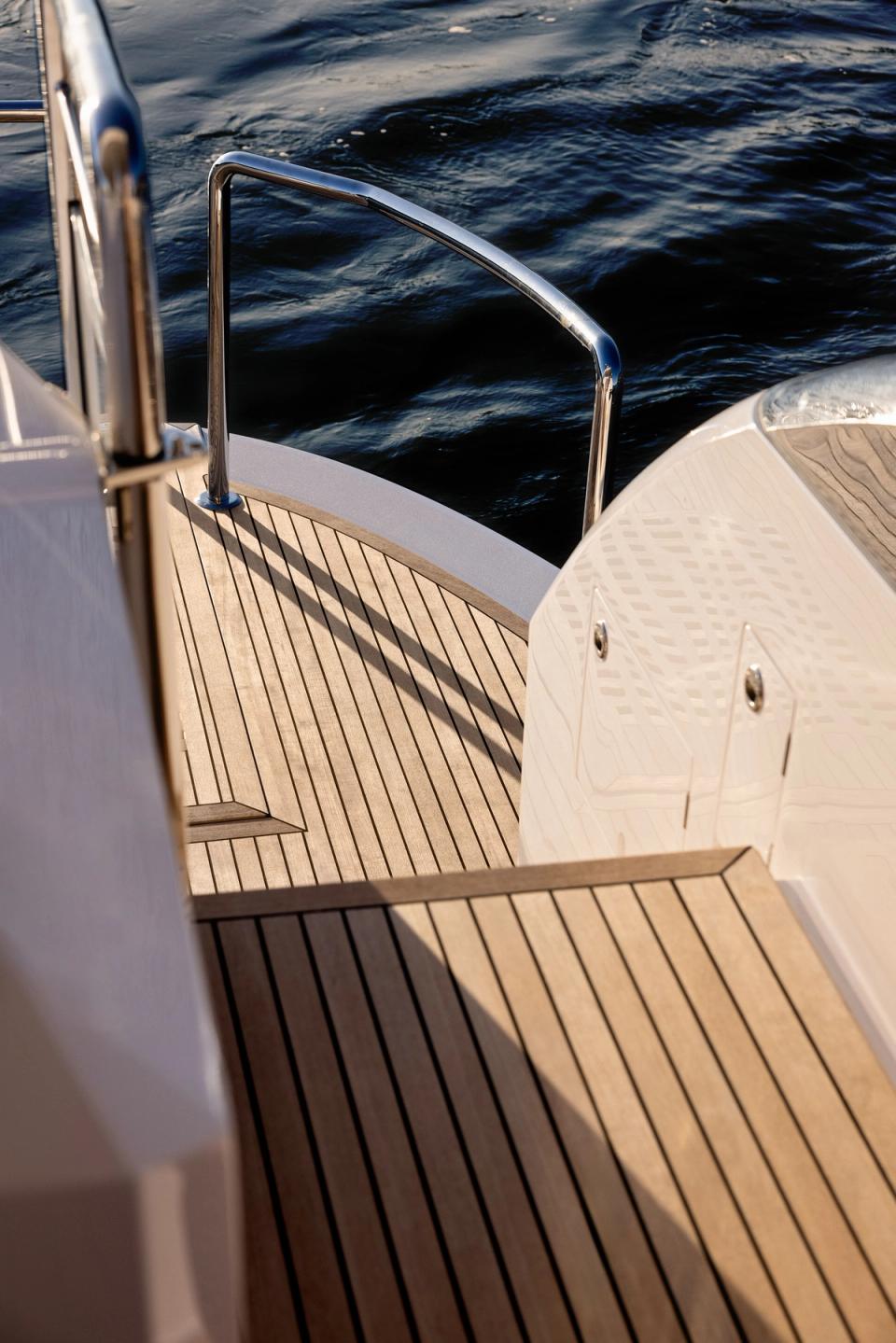 A curved teak swim platform and stern railing overlooking dark water