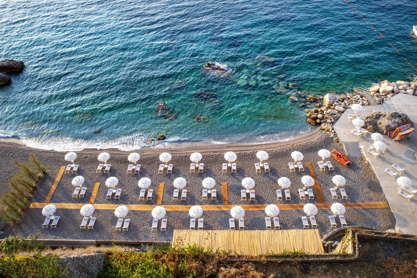 The private beach club at Borgo Santandrea, rows of white parasols above a calm bay