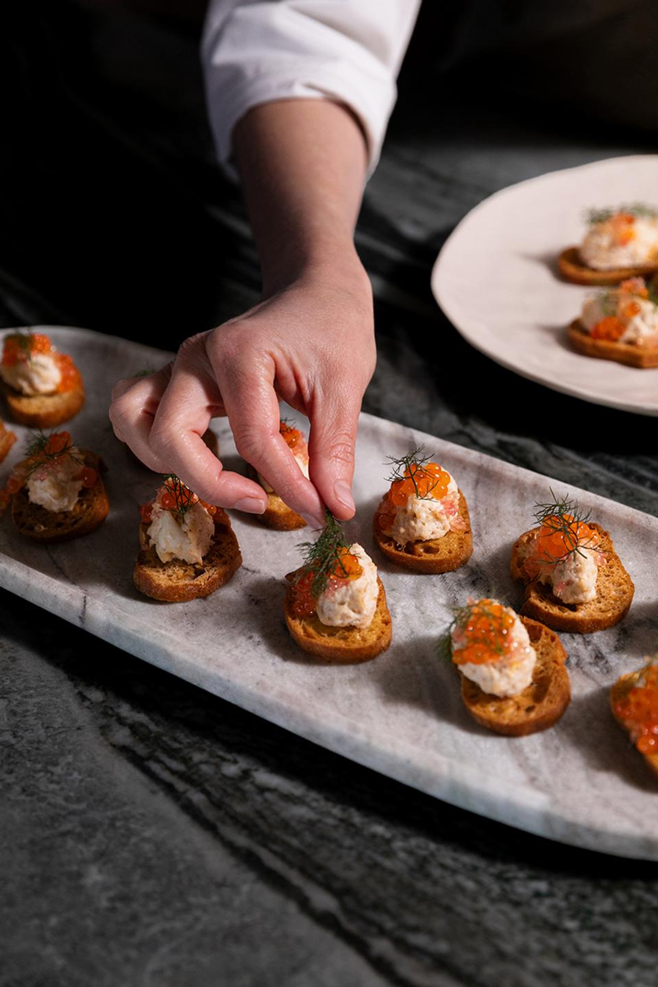 A hand garnishing crostini with dill on a marble serving board